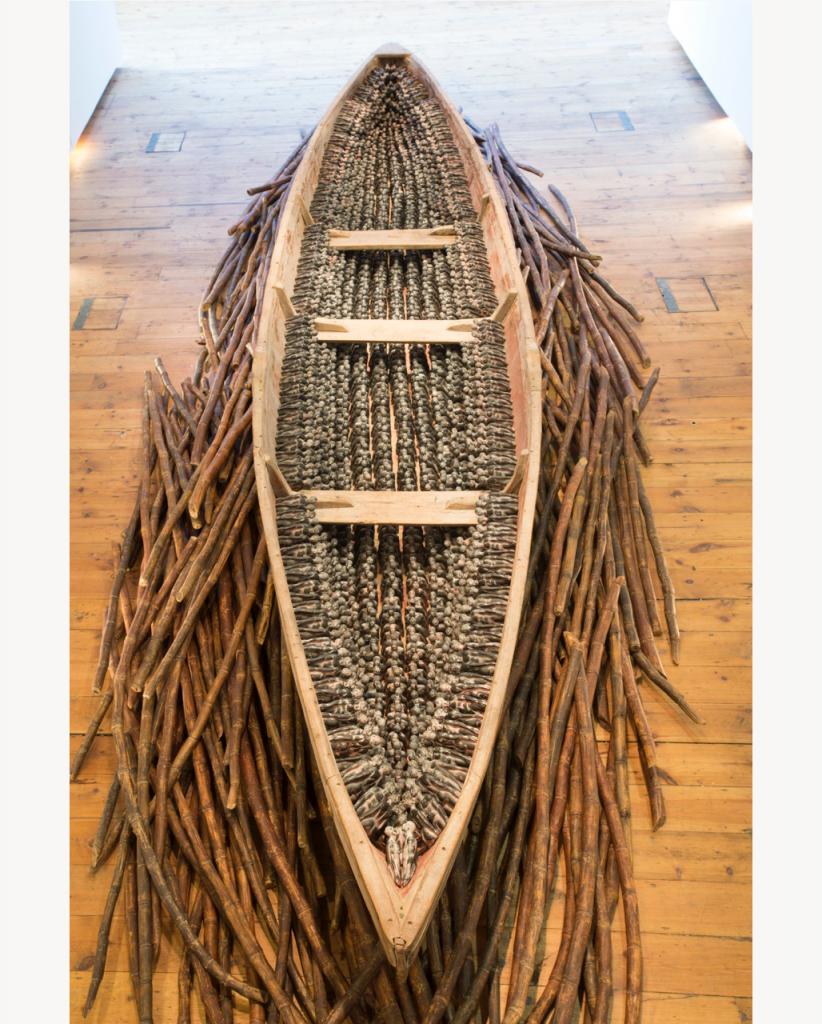 THEIR SPIRITS GONE BEFORE THEM, overview, 2006, cottonwood canoe, 1,357 resin miniatures of the Redemption Song monument, dried sugar cane, 72 x 240 x 33 inches.
